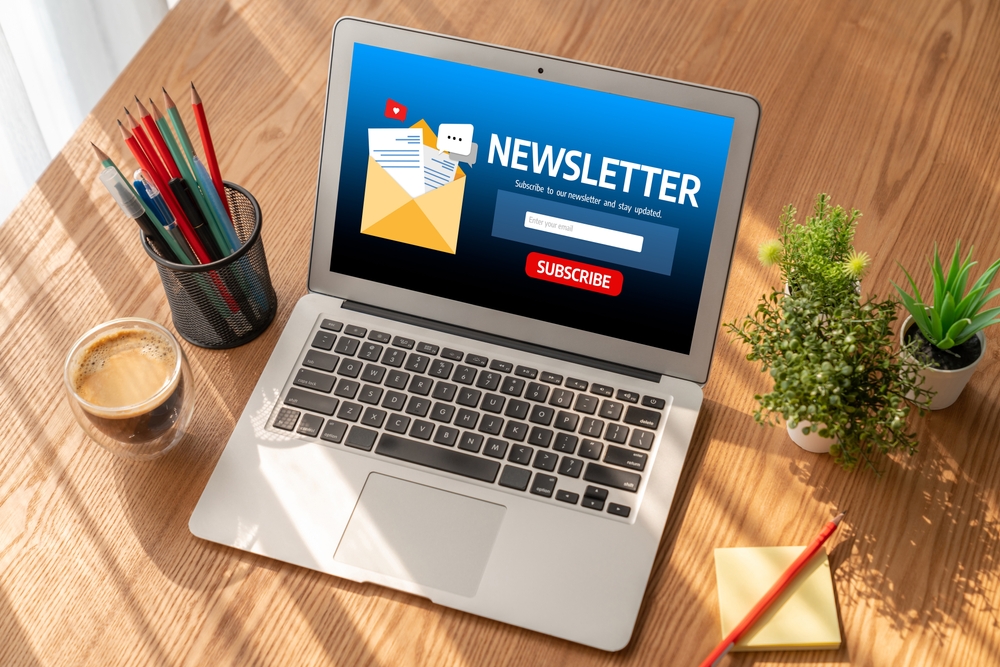 Laptop displaying newsletter interface on wooden desk workspace