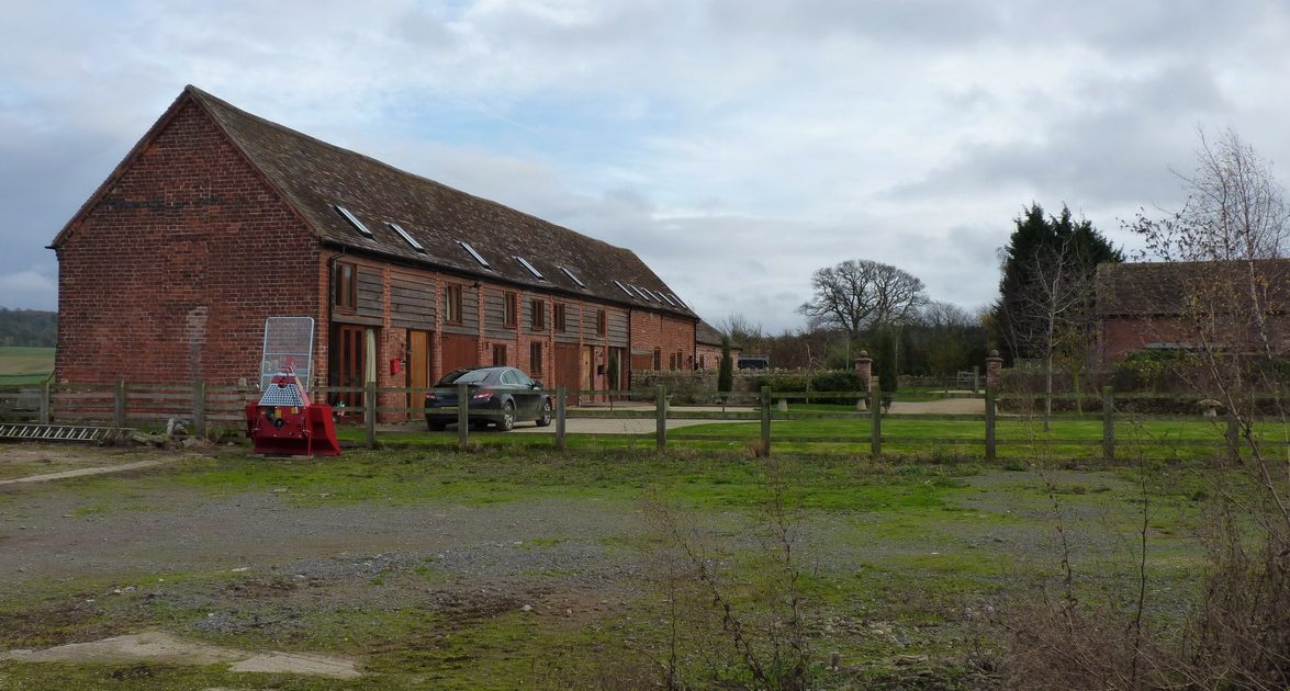Red brick barn conversion with wooden doors and skylights in rural countryside setting